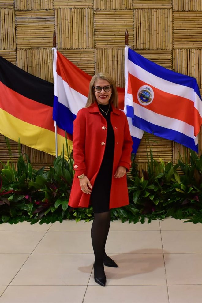 Cynthia Noguera con tapado rojo frente a las banderas en un encuentro internacional